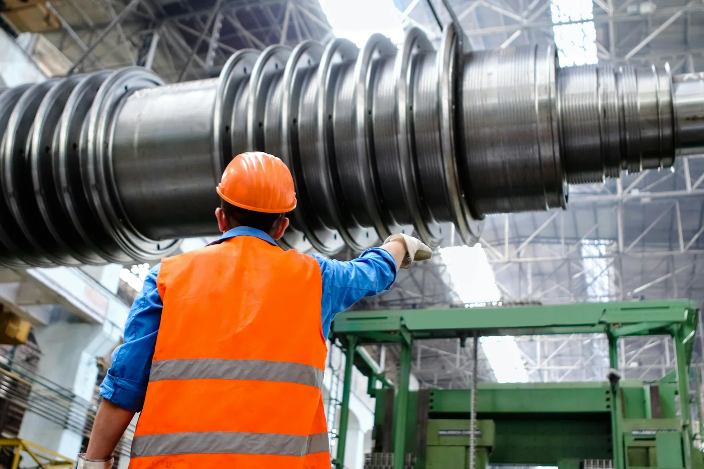 A worker in high-visibility clothing inspects a colossal piece of machinery in an industrial facility.